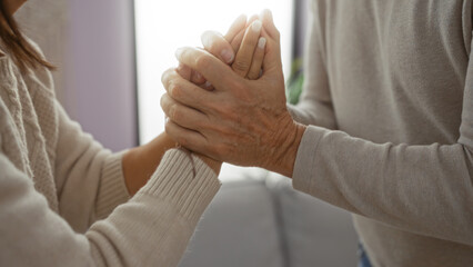 Elderly hispanic couple holding hands indoors, symbolizing love and connection in a cozy home...