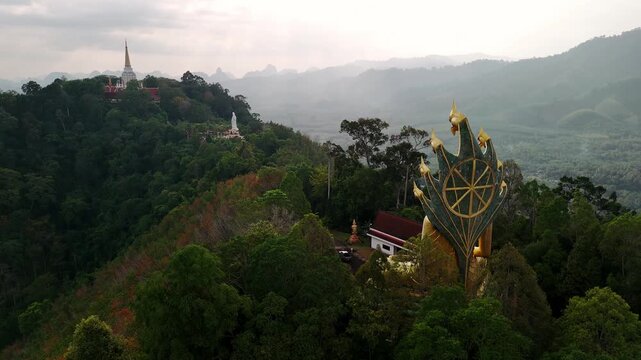Golden budda statue of Wat bang riang temple gleaming under sunlight, standing majestically inside tranquil temple grounds near verdant forest landscape in Phang nga, Thailand.