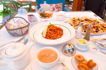 Outdoor lunch table set-up with Italian food. Restaurant dining with seafood pasta, Capricciosa pizza, bread basket, butter, cup of coffee, pot of tea