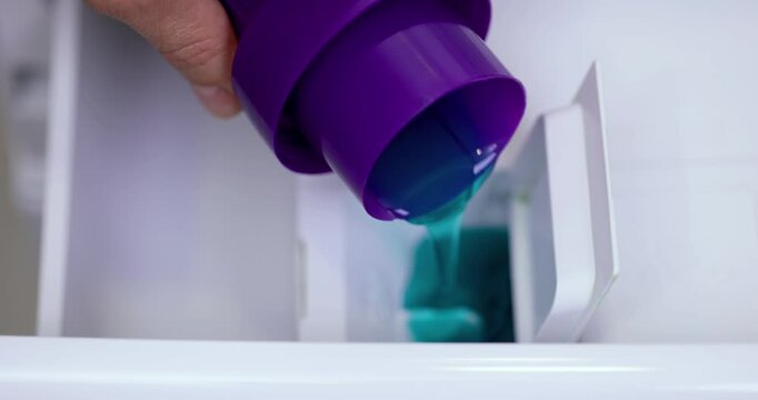 female hand pours liquid laundry detergent into compartment of washing machine, close-up