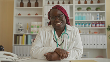 Woman doctor smiling in clinic office with stethoscope and files in background, suggesting a...