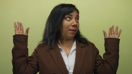 African american woman shrug hands and lift palms wearing brown blazer in studio against light...