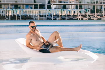 A freelancer works online on a laptop while lying on a sun lounger by the pool, enjoying summer....