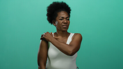 Woman feeling shoulder pain against an isolated green background shows discomfort and tension in a...