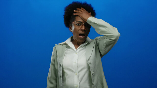 Woman surprised african american wearing glasses isolated on blue background with hands on head and expressing shock or disbelief in studio setting. - Powered by Adobe