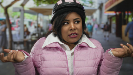 Woman on bike pauses with puzzled expression on city street, wearing helmet and pink jacket near...