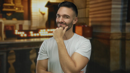 Young man smiling indoors in a dimly lit church setting with candles and religious elements...