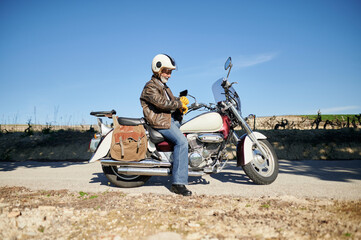 Senior biker wearing gloves sitting on motorcycle parked near vineyard
