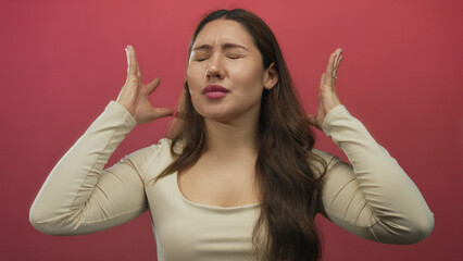 Woman holds head with hands in a pink studio setting showing closed eyes and tense expression;...