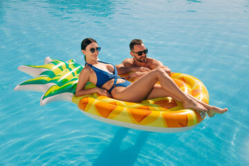 Woman lying on a pineapple float in the pool, young handsome man swimming nearby. Concept vacation,...