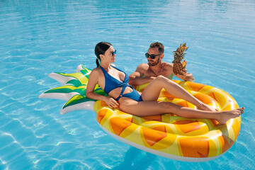 Woman lying on a pineapple float in the pool, young handsome man swimming nearby. Concept vacation,...