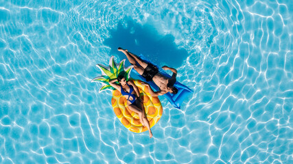 Happy young couple relaxing on inflatable floats in an outdoor pool, enjoying vacation, drone view. Concept love, summer joy, leisure, freedom and tropical mood.
