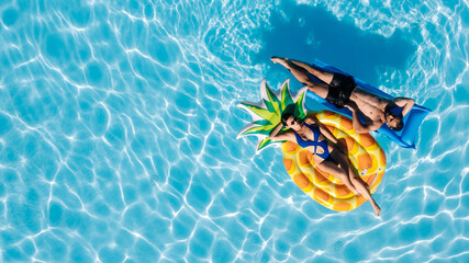 Happy young couple relaxing on inflatable floats in an outdoor pool, enjoying vacation, drone view. Concept love, summer joy, leisure, freedom and tropical mood.