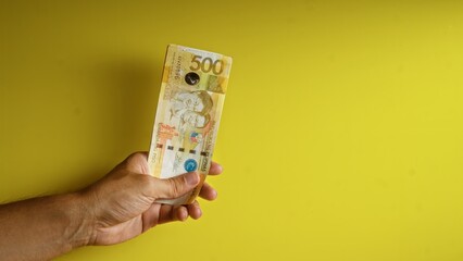 Hand holding a 500 peso philippine banknote against a yellow background, featuring close-up details...