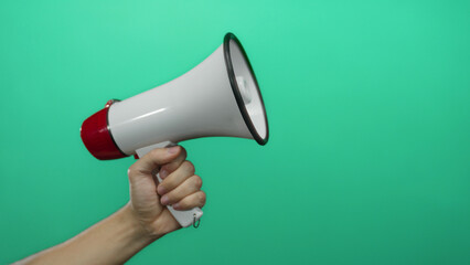 Male hand grasping white megaphone against vibrant green background suggests communication and...