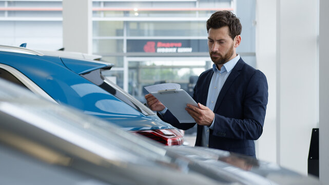 Caucasian man reading documents manager salesman consultant advisor specialist work clipboard car auto automobile dealer male businessman business seller agent checking papers guy electric transport