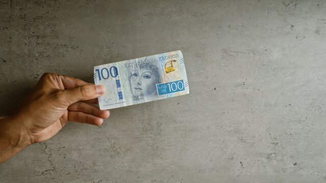 Man holding swedish 100 krona note against concrete background, highlighting currency and financial themes in sweden.