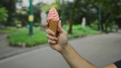 Man holding ice cream cone outdoors on a city street with pink ice cream in a park setting amidst...