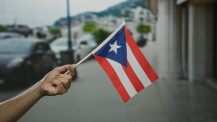 Hand of a man holding a puerto rico flag in an outdoor city setting, showcasing national pride and...