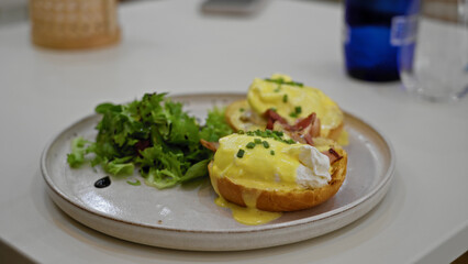 Person eating eggs benedict with fresh salad in a cozy restaurant setting, highlighting delicious brunch cuisine and indoor dining experience.