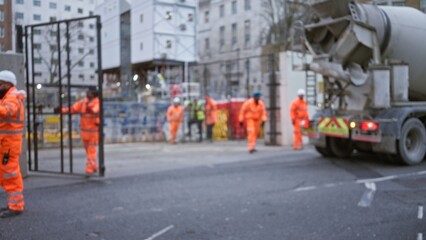 Construction workers in orange uniforms at blurred construction site with bokeh effect, concrete...