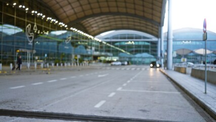 Blurred airport scene with defocused architecture and bokeh lights, featuring a traveler pulling luggage outside terminal amidst an overcast outdoor setting with reflective surfaces.