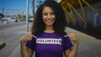 Woman pointing to volunteer shirt on urban street emphasizes community involvement outdoors.