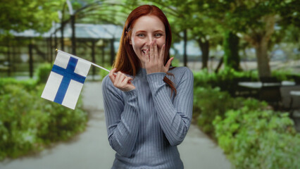 Woman holding finnish flag in park with redhead hair smiling in outdoor setting showcasing national...