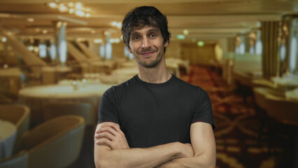 Obraz premium Man crossing arms and smiling broadly at camera in restaurant dining room under warm lighting; confidence joy.