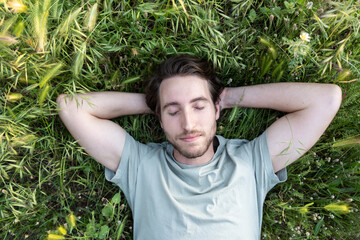 A man lying on green grass with eyes closed and peaceful expression