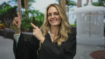 Woman judge outdoors in park pointing and smiling wearing black uniform and glasses amidst green...