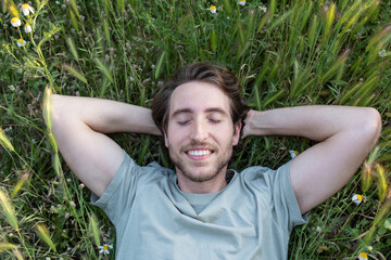 A man lying on green grass with eyes closed and peaceful expression