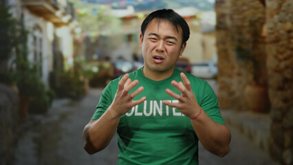 Young man wearing green shirt with 'volunteer' text gestures emotionally in a charming urban street...