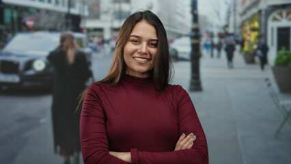 Woman with crossed arms smiles confidently on a busy urban street, blending modern style with...