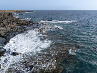 View of a rocky beach in the south of the island of Tenerife on a beautiful sunny day, waves crashing on the rocks, horizon over sea