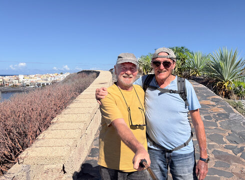 Cheerful couple of two senior men with hat on outdoor hike taking a picture with a selfie stick. Relaxed and serene retirement lifestyle