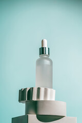 A frosted dropper bottle of facial serum is placed on a sculpted white pedestal with a soft teal...