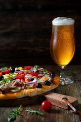 Homemade pizza with champignons and black olives and a glass of chilled beer on a rustic table