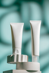 Two white tubes of soothing face cream stands on a sculpted pedestal against light aqua background....