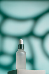 A frosted dropper bottle of facial serum is placed on a sculpted white pedestal with a soft teal...