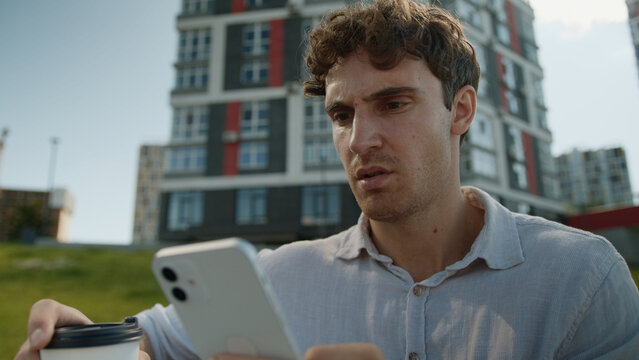 Frustrated Caucasian man reading bad news mobile phone smartphone cellphone male businessman stressed nervous guy city message error connection problem worried business outdoors holding cup coffee app