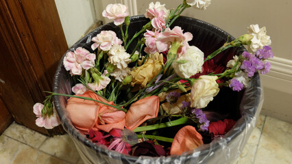 A bouquet of flowers in different varieties, thrown away into a rubbish bin. 