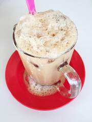 Closeup of a glass of iced teh tarik, a pulled milk tea beverage that is popular in Malaysia.