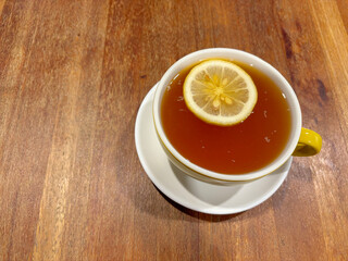 A full cup of English tea, with a slice of lemon floating on top. On a wooden table.