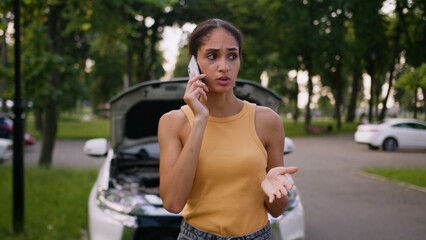Anxious African American woman driver talking mobile phone breakdown car open bonnet accident...