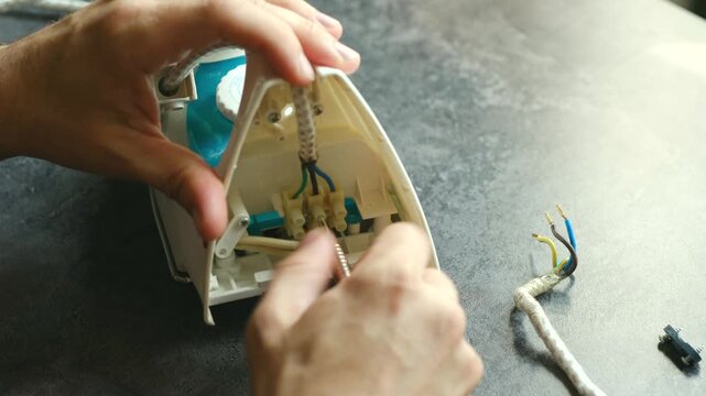 Close up shot of technician hands use screwdriver carefully reconnecting power cable to an iron, showcasing intricate process of electrical repair. Technician repairing broken iron cable connection