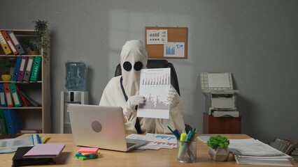 Halloween businessman ghost in white sheet with necktie sitting at office desk shows financial graphs on laptop video conference. Happy halloween business concept.