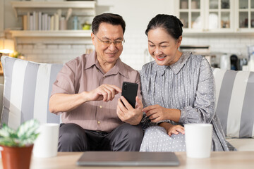 Asian senior couple enjoy using mobile phone on sofa. grandparent learning and connecting with...