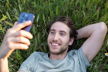 Happy man using his mobile phone relaxing in the green grass in summer