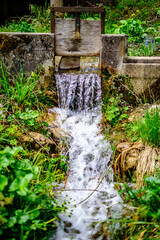 Flowing water cascades over the gates of a hydroelectric dam in a scenic landscape at midday,...
